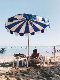 People sitting on deck chairs at beach against sky