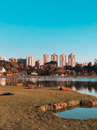 Lake by buildings against clear blue sky