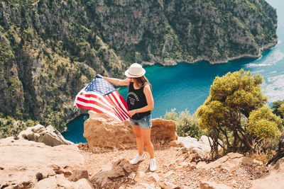 Woman standing on rock and waving  us flag. traveler standing on mountain. 4 july independence day