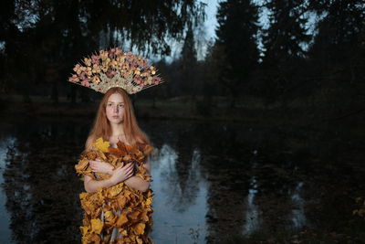Young woman looking away while wearing headdress by lake in forest