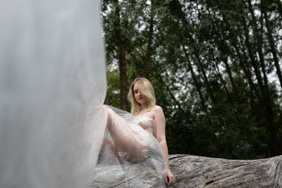 Young naked woman sitting on tree trunk in forest