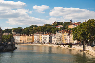 Bridge over river by buildings in city against sky