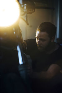 Young man repairing illuminated motorcycle in garage