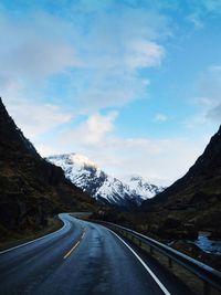 Empty road leading towards mountains against sky