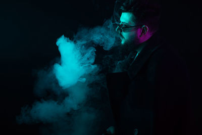 Young man smoking cigarette against black background