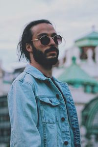 Young male hipster wearing denim jacket and sunglasses against sky