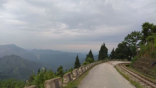 Empty road along trees and plants against sky