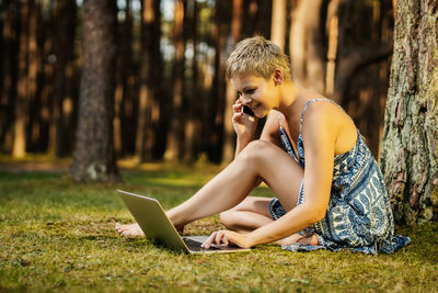 Woman talking on phone while using laptop in forest