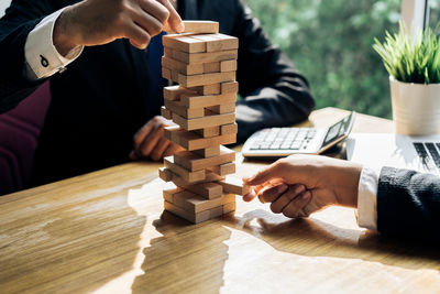 Midsection of businessmen stacking wooden blocks on office desk