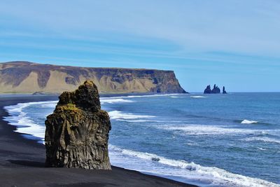 Rock formation on black sand beach against sky