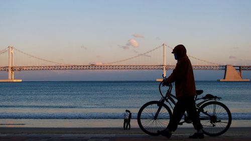 Full length of man walking with bicycle against bridge over river