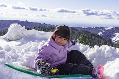 Girl sitting on snow covered landscape against sky
