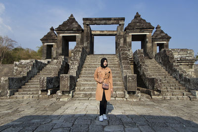 Muslim tourist woman wearing hijab / headscarf and brown coat at ratu boko temple, yogyakarta