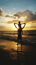 Silhouette father carrying son on shoulders at beach during sunset