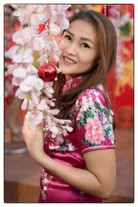 Portrait of a smiling young woman holding red flowering plant