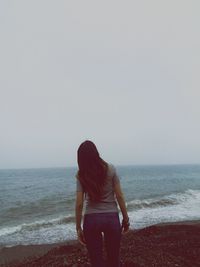 Rear view of woman standing on beach against sky