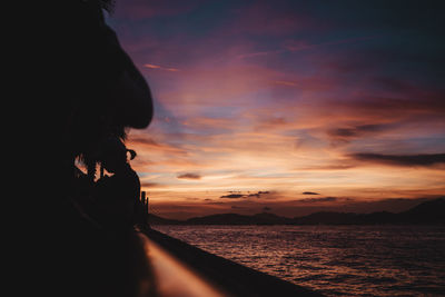 Rear view of woman standing at beach against sky during sunset