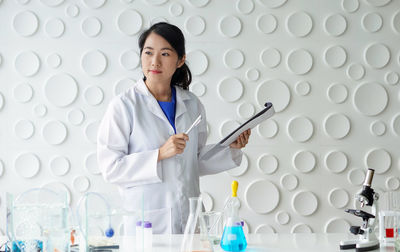 Scientist holding clipboard looking away at lab