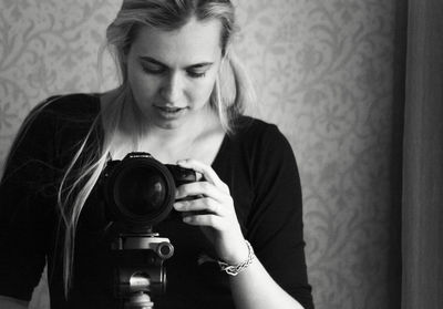 Young woman adjusting camera against wall