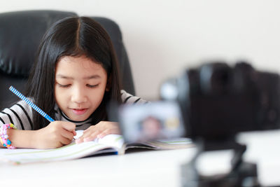 Camera photographing girl writing on book at table