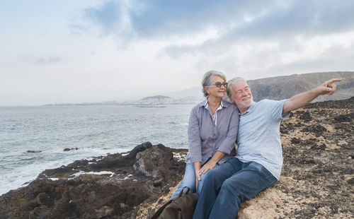 Rear view of couple on rock by sea against sky