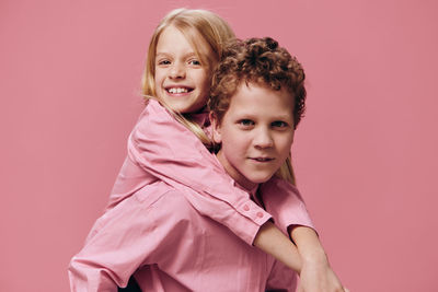 Portrait of boy giving piggyback ride to sister against pick background