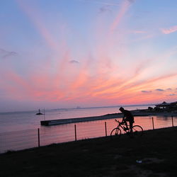 Silhouette people riding bicycle on beach against sky during sunset