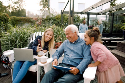 Smiling family using digital technology while sitting in backyard during weekend