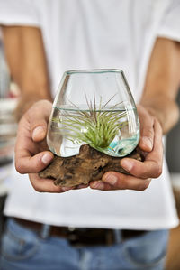 Man holding small plant in glass jar at home