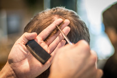 Cropped hands of barber cutting man hair