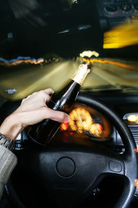 Cropped hand of woman holding beer bottle driving car