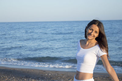 Smiling young woman standing on beach against sky