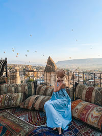 Rear view of woman sitting on retaining wall against sky