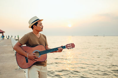 Man playing guitar at beach during sunset