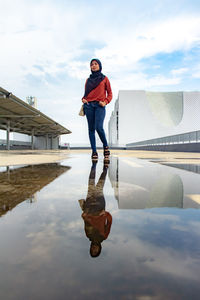 Full length of woman standing by puddle against sky