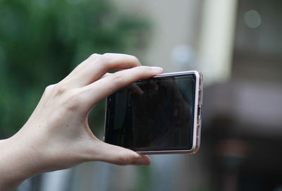 Cropped hand of woman photographing with phone in city