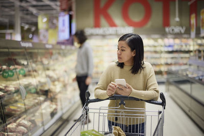 Woman doing shopping in supermarket and holding cell phone
