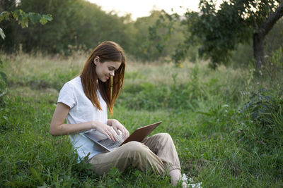 Young woman using laptop while sitting on field