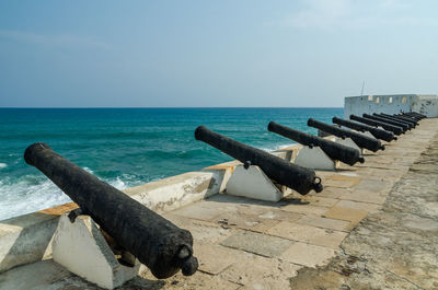 Scenic view of old cannons at cape coast castle on sea against sky, ghana