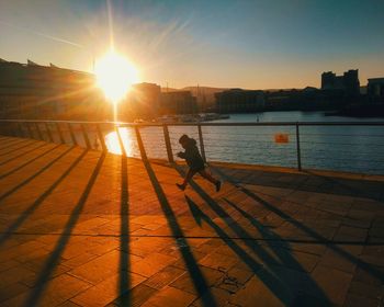 Silhouette person by sea against sky during sunset in city