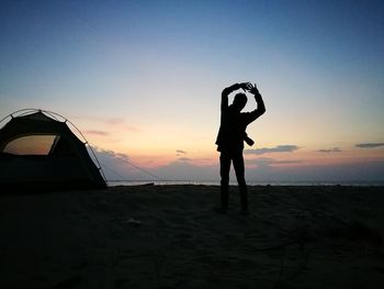 Silhouette man standing on beach against sky during sunset