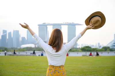 Rear view of woman with arms raised standing against sky