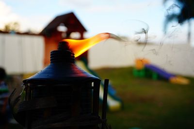 Close-up of lit oil lamp in yard against sky