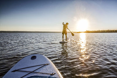 Man standing in sea against sky during sunset