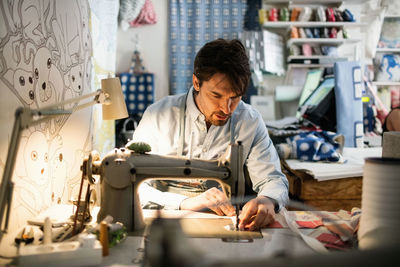 Serious owner sewing fabric at shop