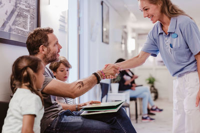 Smiling female doctor greeting man waiting with son and daughter in hospital corridor