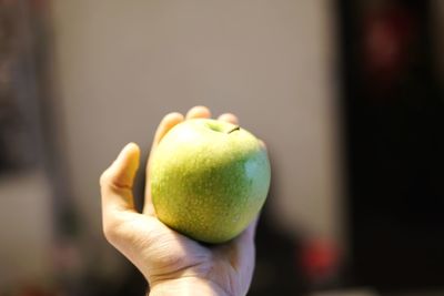 Cropped hand holding granny smith apple at home