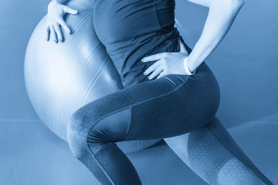 Low section of woman sitting against blue background