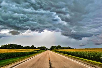 Road passing through field against storm clouds