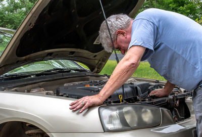 A senior male works under the hood of his car to repair a mechanical issue